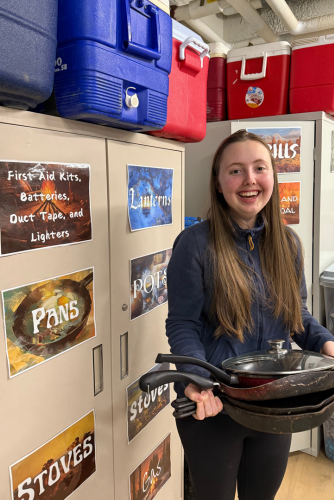 Ava Ward holding a stack of frying pans in the newly-labled gear room.