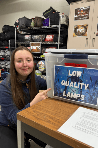 Ava Ward pointing to a box of Low Quality Lamps in the gear storage room. 