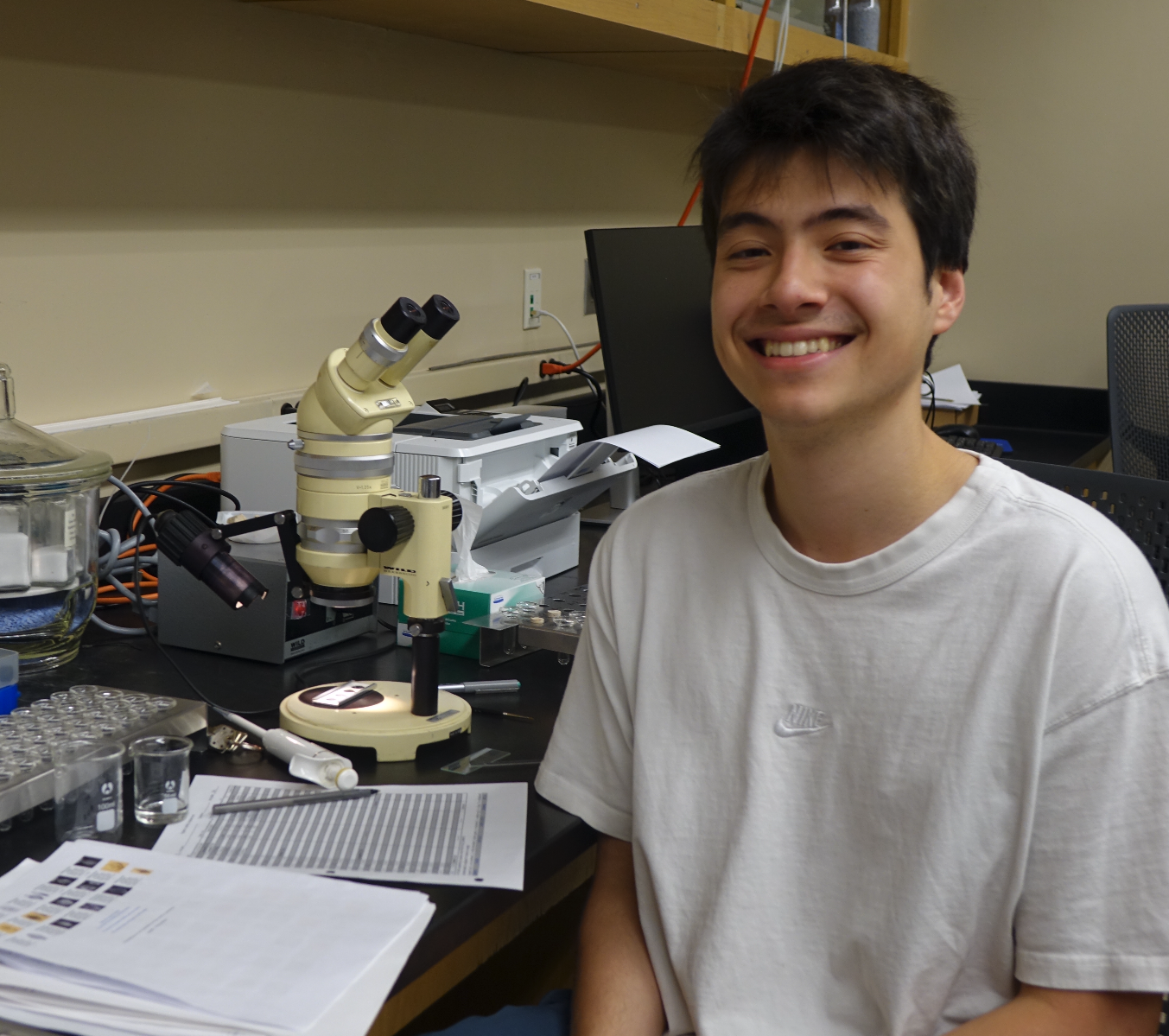 Galen in the lab, smiling beside the microscope and samples. 