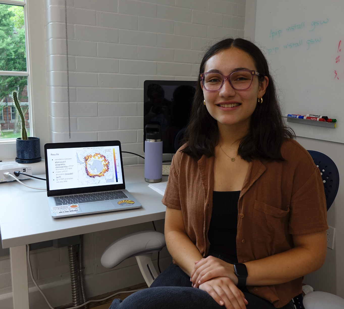 Margaret smiling for the photo beside a laptop with her project results presentation.