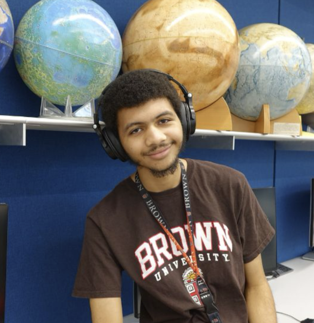 WaTae smiling for a photo beneath a shelf of planet models. 