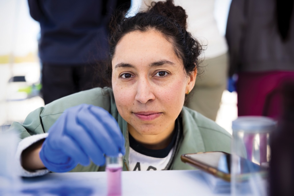 Alejandra Lopez on site at the Salton Sea data collection project, wearing blue gloves in front of a table of water samples