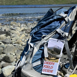 The DEEPS Field Preparedness Guide printout strapped to a hiking backpack on a rocky river bank