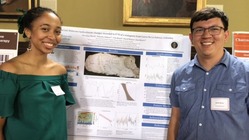 A student and professor standing at a research poster smiling for the photo. 