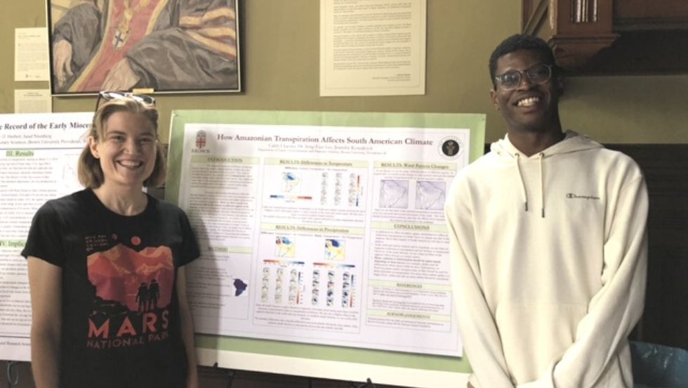 Two students standing at a research poster smiling for the photo.