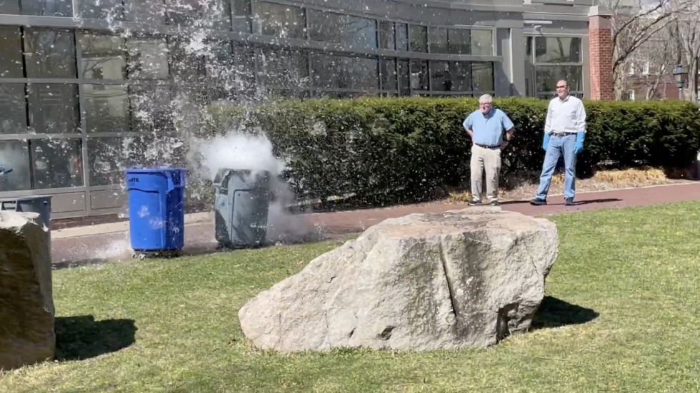 Two DEEPS volunteers watch as water erupts from the trash bin. 