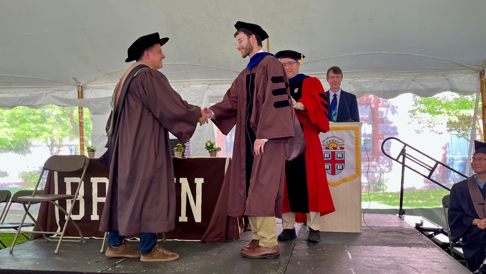 Ethan Kyzivat shaking the hand of Brown Corporation Member receiving his diploma. 