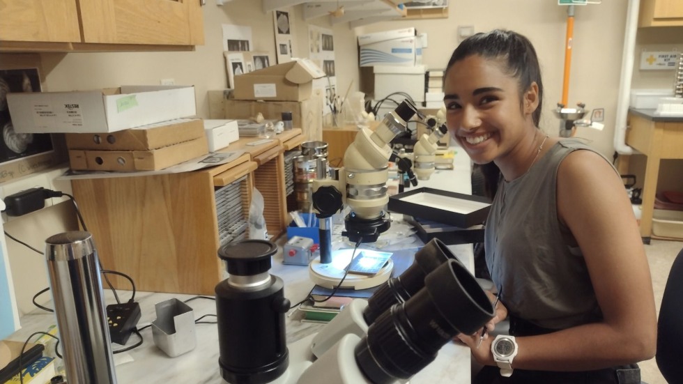 Anjali smiling beside a microscope. 