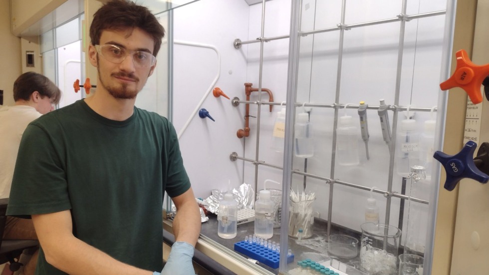 Gabriel posing for a photo beside a lab work station. 