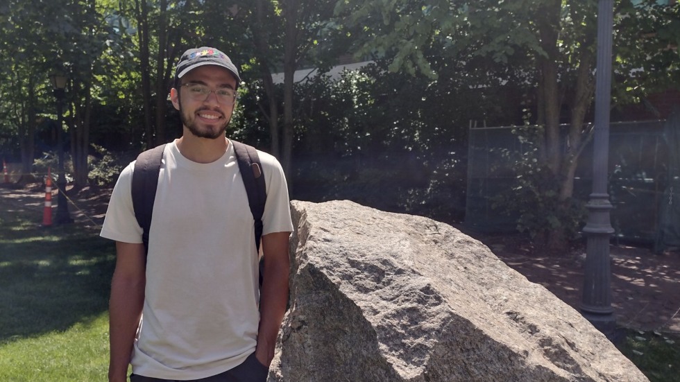 Isaiah smiling for a photo beside a boulder on Brown's campus. 