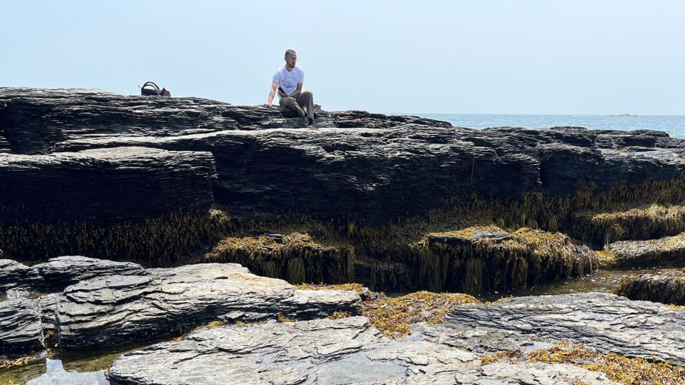 Isaiah sitting on a stone beside the ocean. 