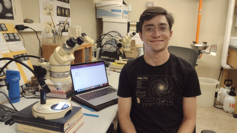 Maxwell smiling for the photo sitting in the lab beside a microscope. 