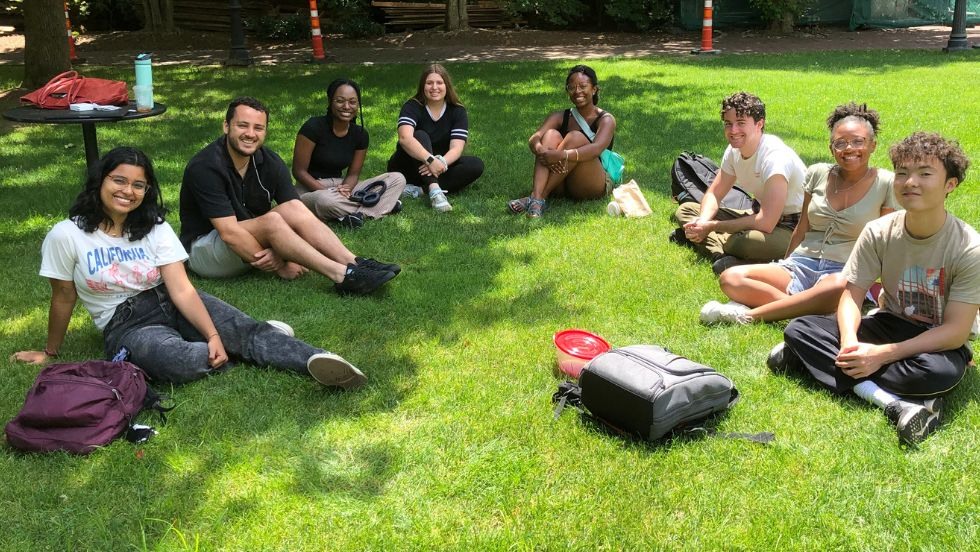 The 2023 REU cohort sitting on the grass on a sunny day.