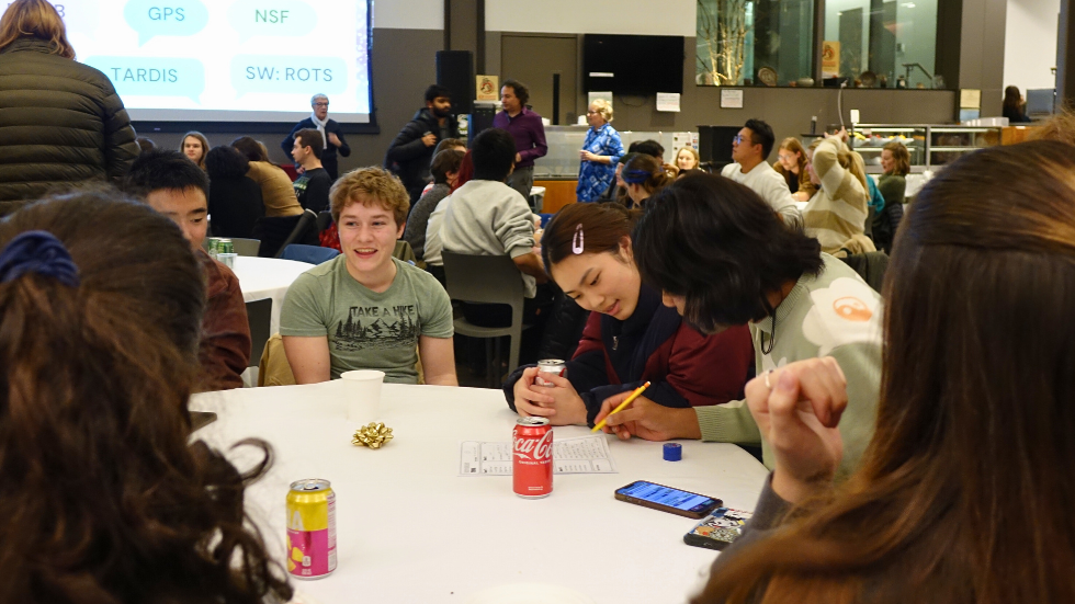 A candid photo of students talking together and filling out the trivia game sheet.