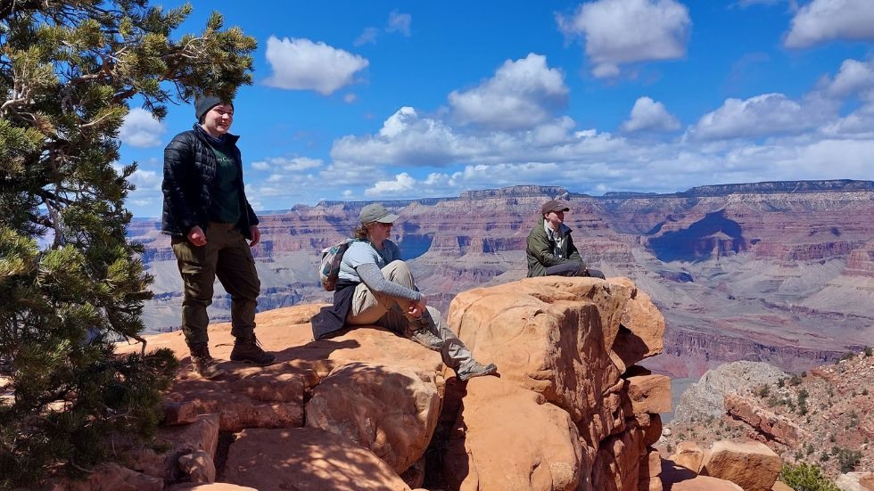 Three students sitting together on a ledge over the canyon