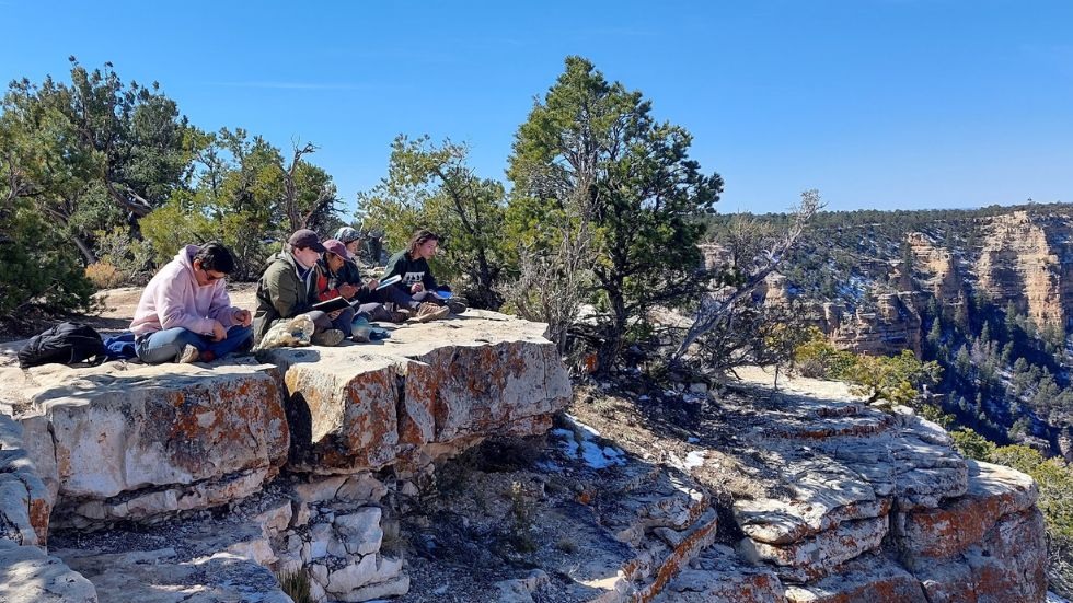 students sitting on a ledge drawing the canyon view