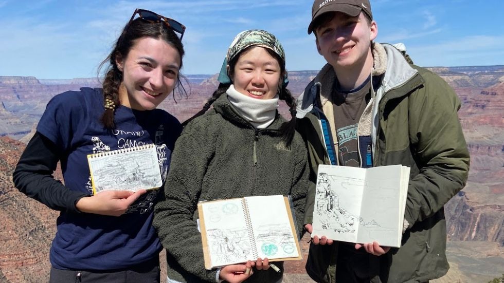 three students present their sketchbooks with drawings of the canyon