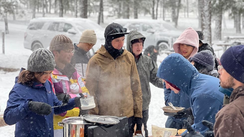 Students cooking on a grill at the campsite while it snows