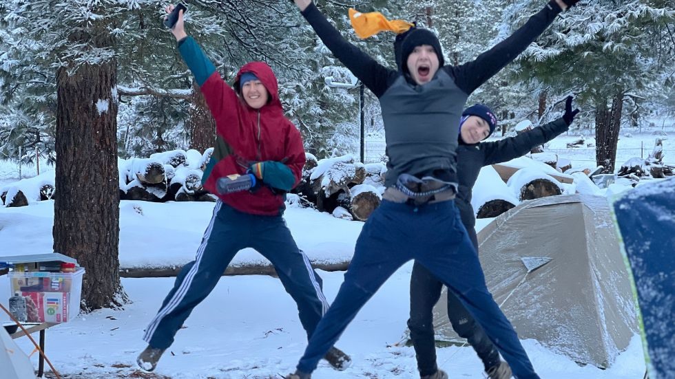 Three students jumping in the air at the snowy campsite. 