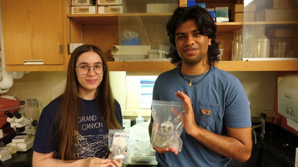 Shannon White and Dev Patel holding rock samples in bags 