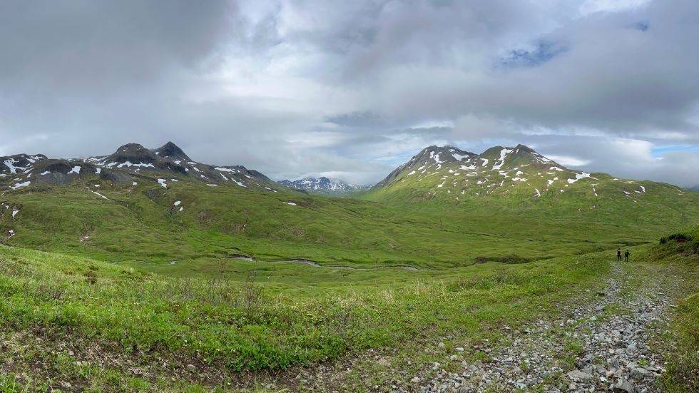 A wide scenic photo of the alaskan landscape, with Anahi Carrera and Emily Cooperdock hiking away