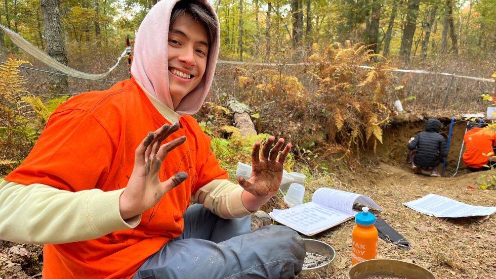 a student smiles while showing off his hands covered in dirt 