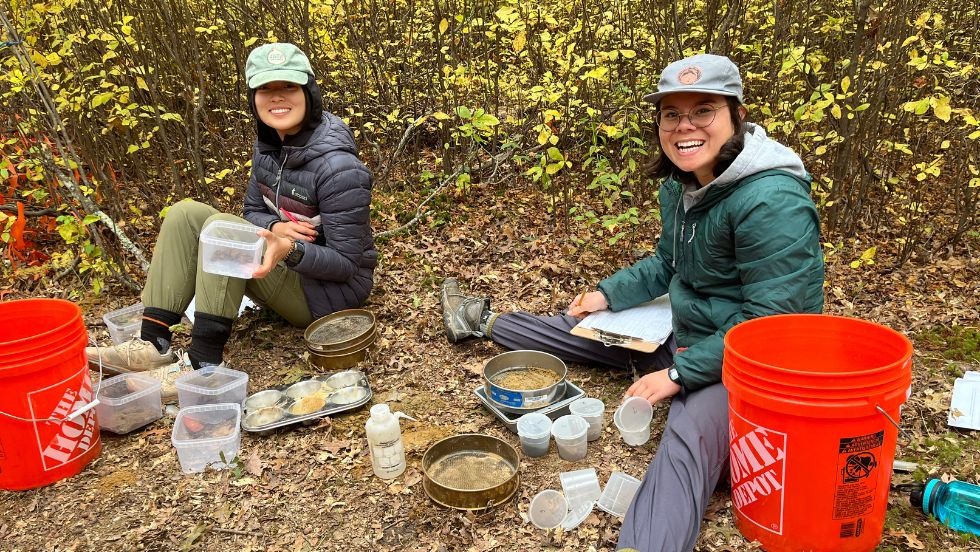 two students smile while reviewing soil samples