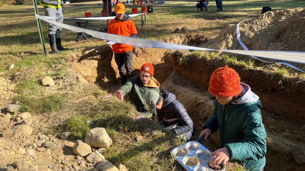 students in a hole in the ground taking soil samples