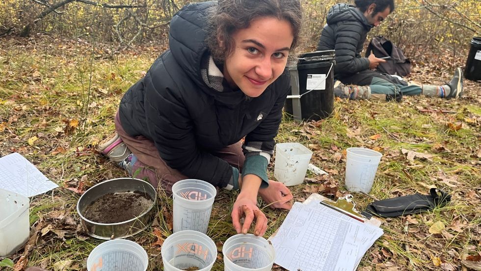 a student measuring soil samples in cups on the grass