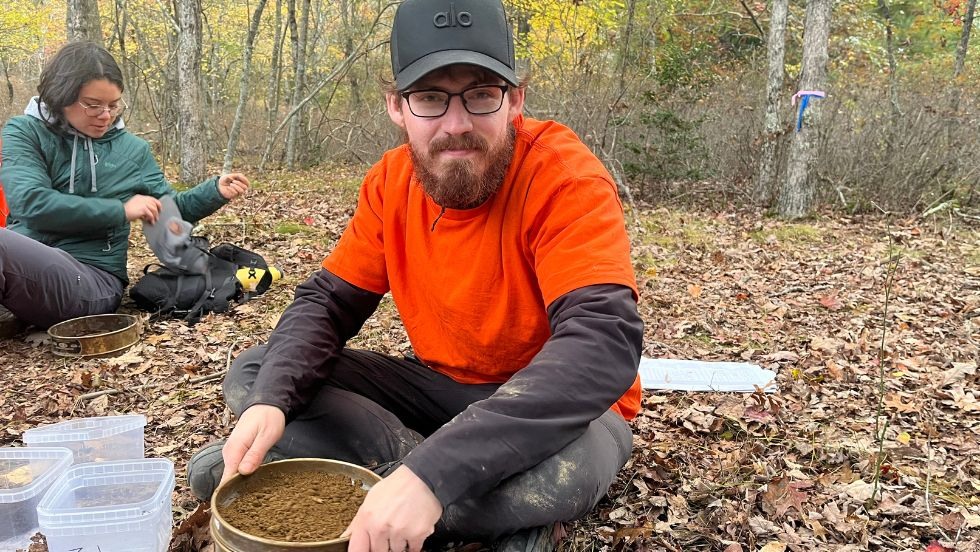 a student smiles while reviewing soil samples on the grass