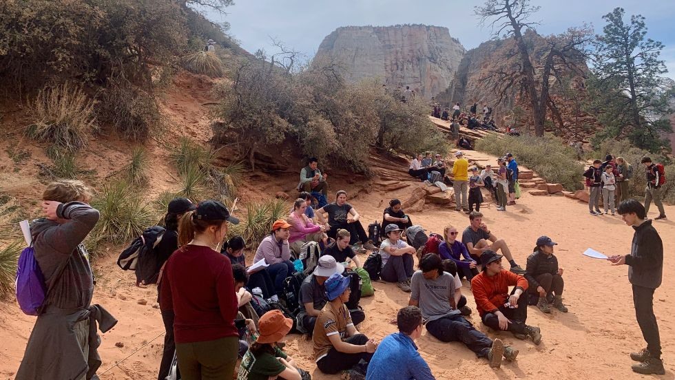 students sit and listen to their peer present geologic info about the nearby landscape