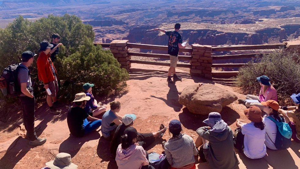 students sit and listen to their peer present geologic info about another landscape