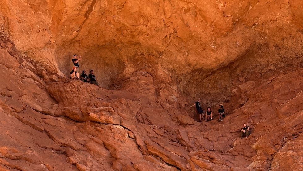 students hiking up a red desert stone cliff face