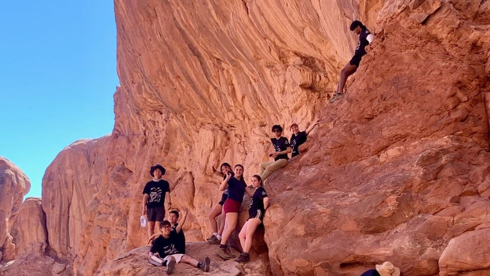 students smile and wave while climbing up red rock formations