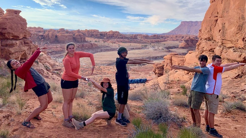 students posing to spell out S B F T in front of a desert scene