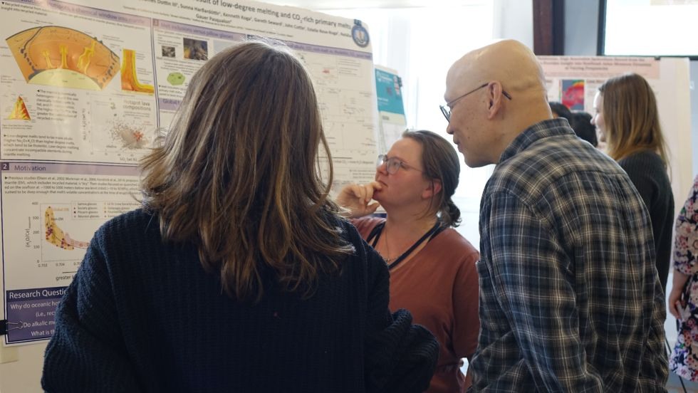 a graduate student discusses her research poster with peers and faculty 