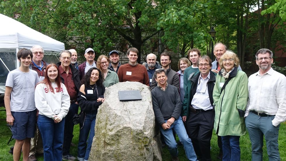 guests pose in a group around the new plaque honoring Jan on the stones outside Geochem 