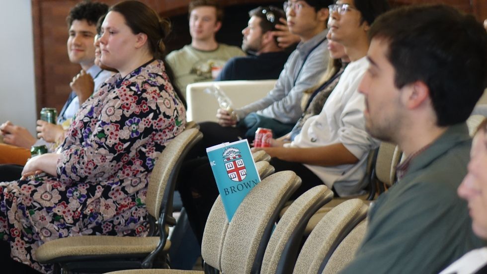 we can see a rolled research poster with the Brown logo resting between seats while attendees listen to a talk
