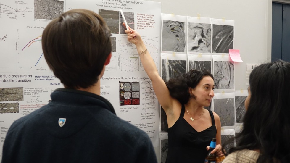 a grad student reaches to point to the top of her poster in a crowded hallway