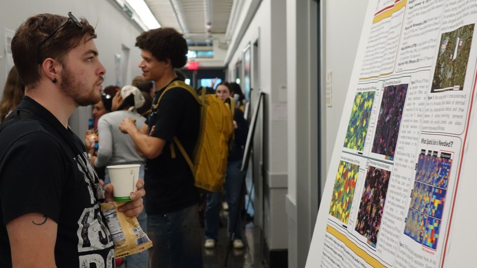 a new grad student looks at a poster in the crowded hallway