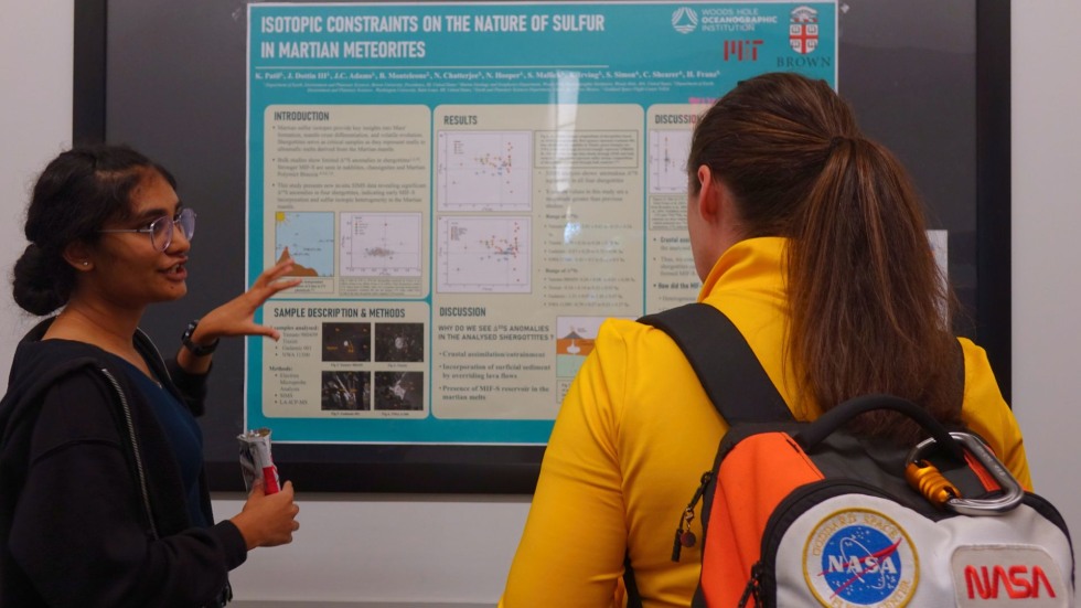 a student discusses her poster with another student in a NASA backpack