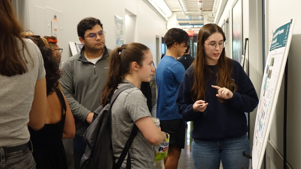 an undergrad discussing her poster with a peer in the crowded hallway
