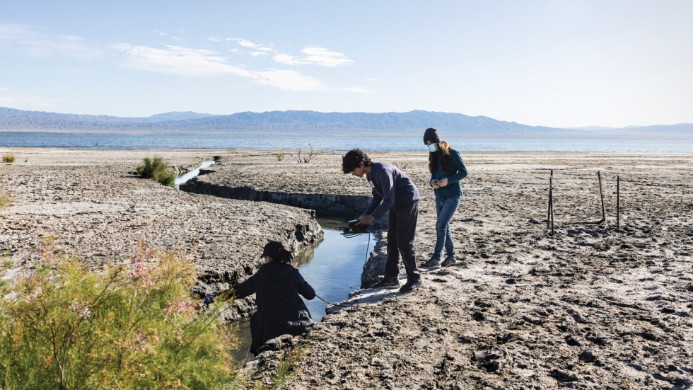 three scientists in shallow creek taking water samples 