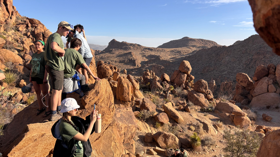 students hiking in the desert rock formations, stopping to take in the view