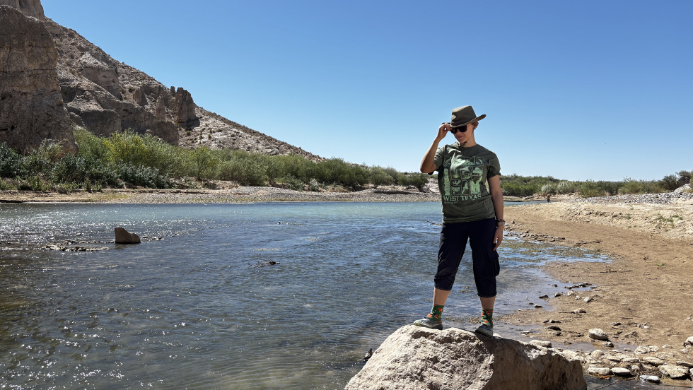 a student poses like a cowboy on a rock beside the river 