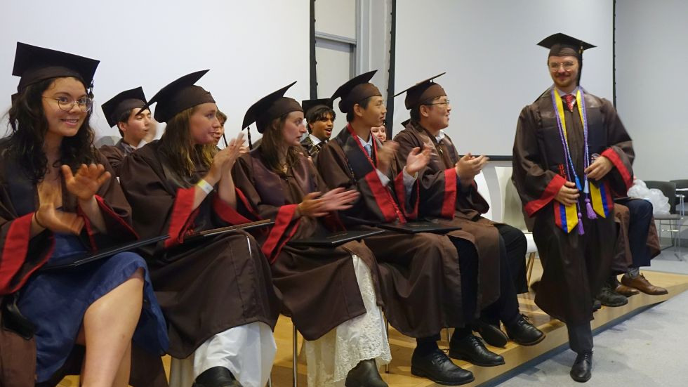 undergrads seated on stage cheer while their peer walks to the front for his degree