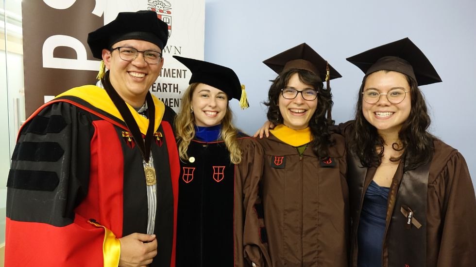 a professor and three graduating students smile for a photo 