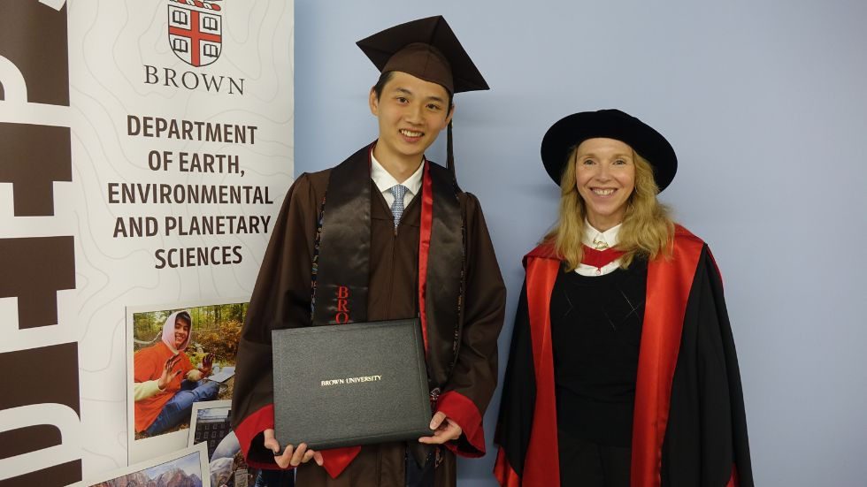 a graduating student his advisor smile beside the DEEPS banner 