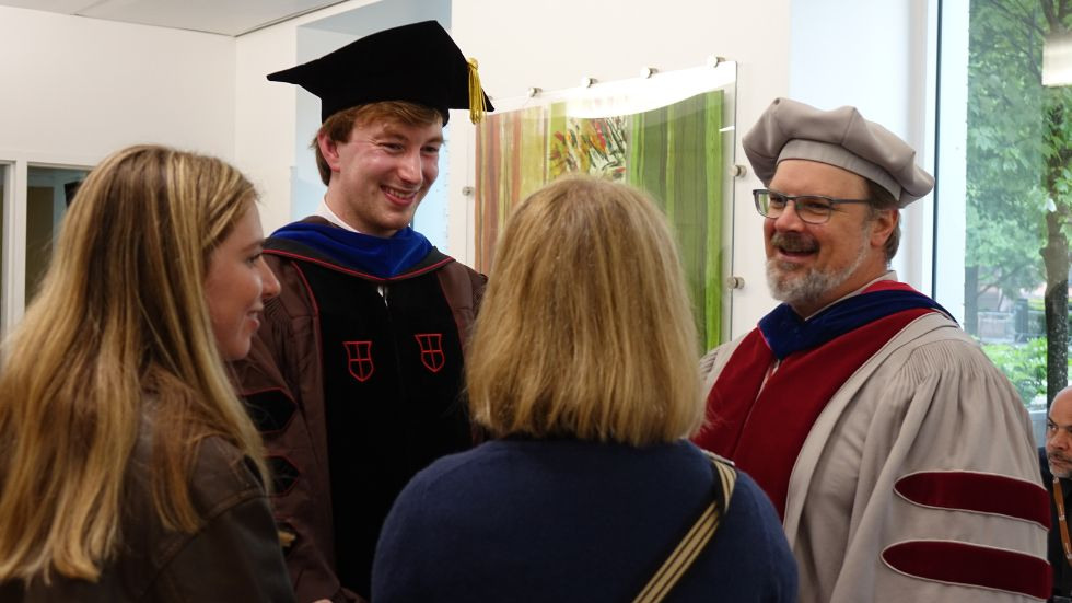 a professor and grad laugh with friends and family at the reception 