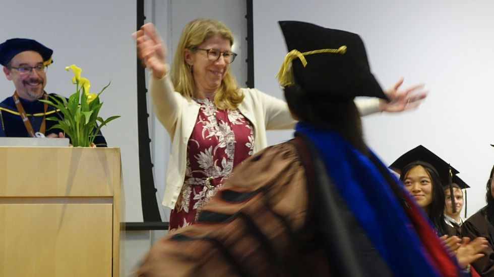 Professor and PhD student hug after bestowing her hood 